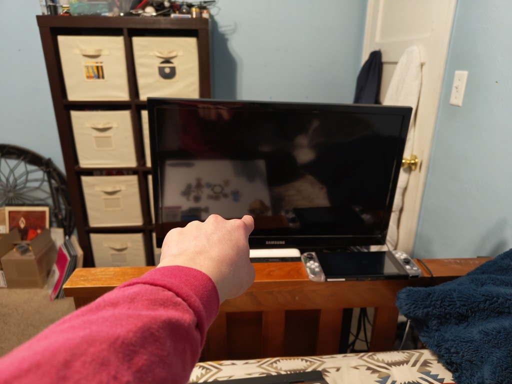 a picture of me pointing at the 24 inch tv at the foot of my bed, sitting atop a tiny night stand